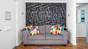 Una sala de estar moderna con un sofá gris, cojines geométricos coloridos, un panel de pared geométrico y piso de madera.