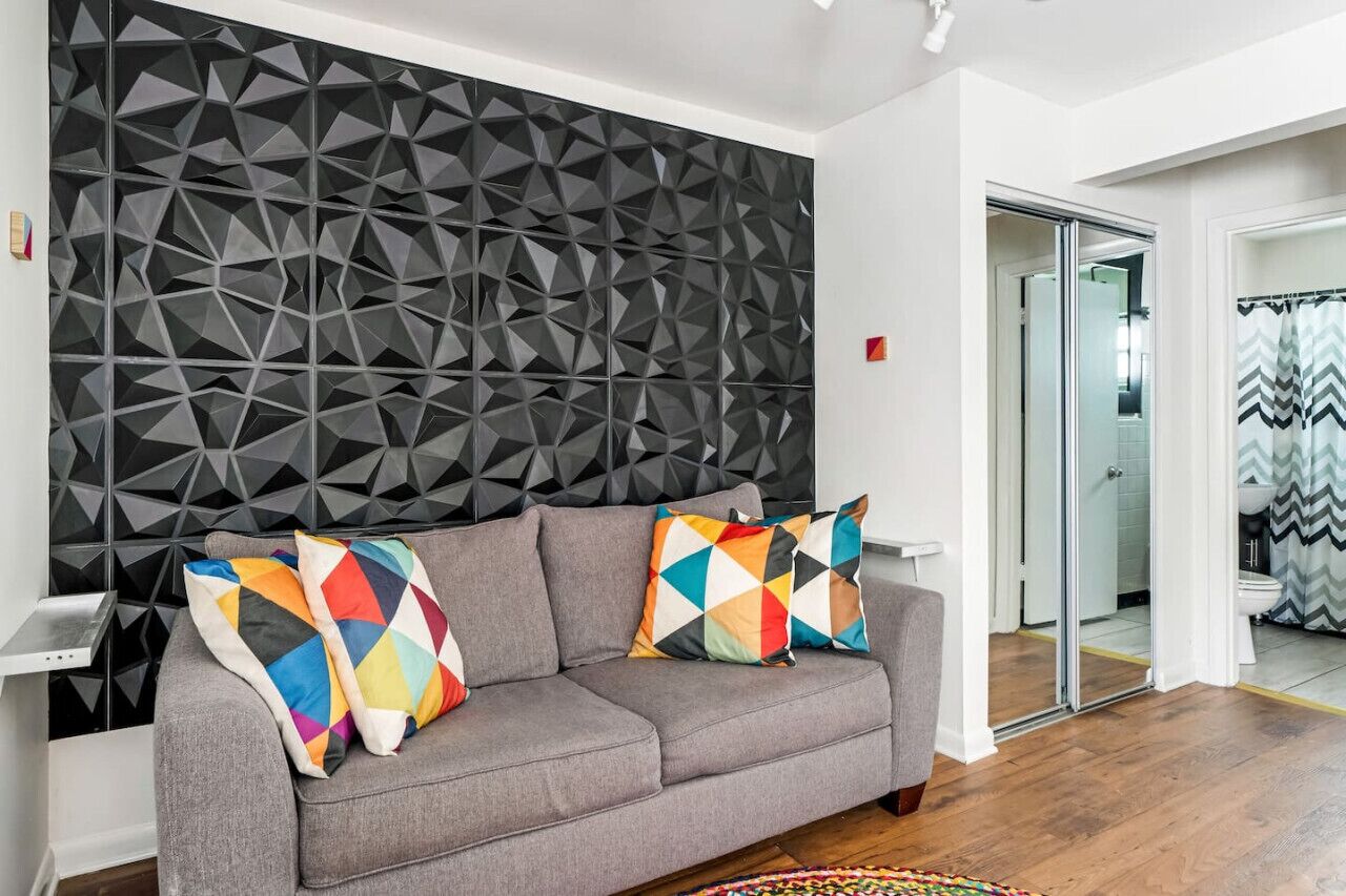 A modern living room with a grey sofa, colorful geometric pillows, and a textured wall.