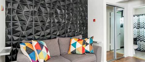 A modern living room with a grey sofa, colorful geometric pillows, and a textured wall.