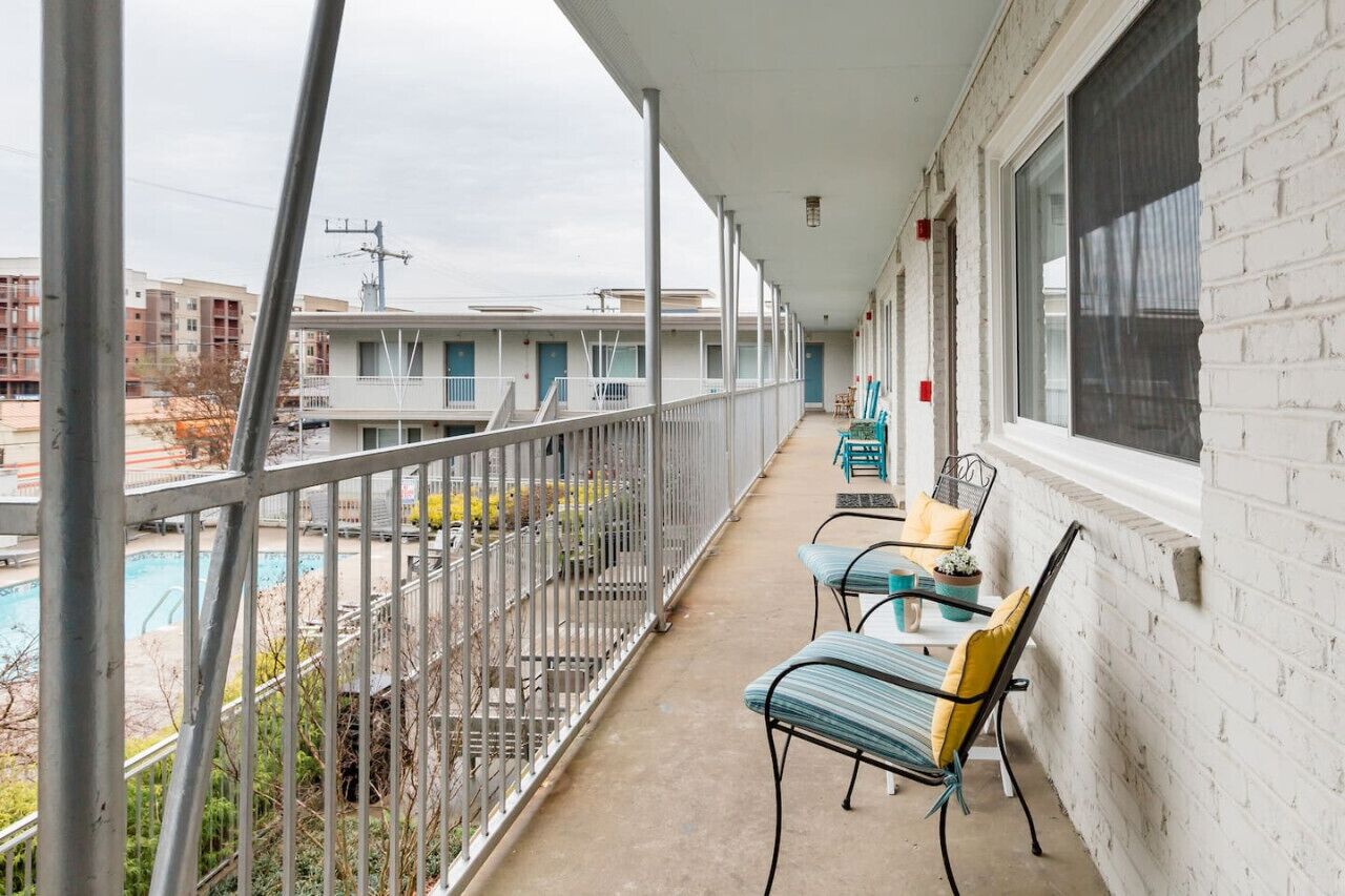 A balcony with a pool, outdoor seating, and a view of other buildings.