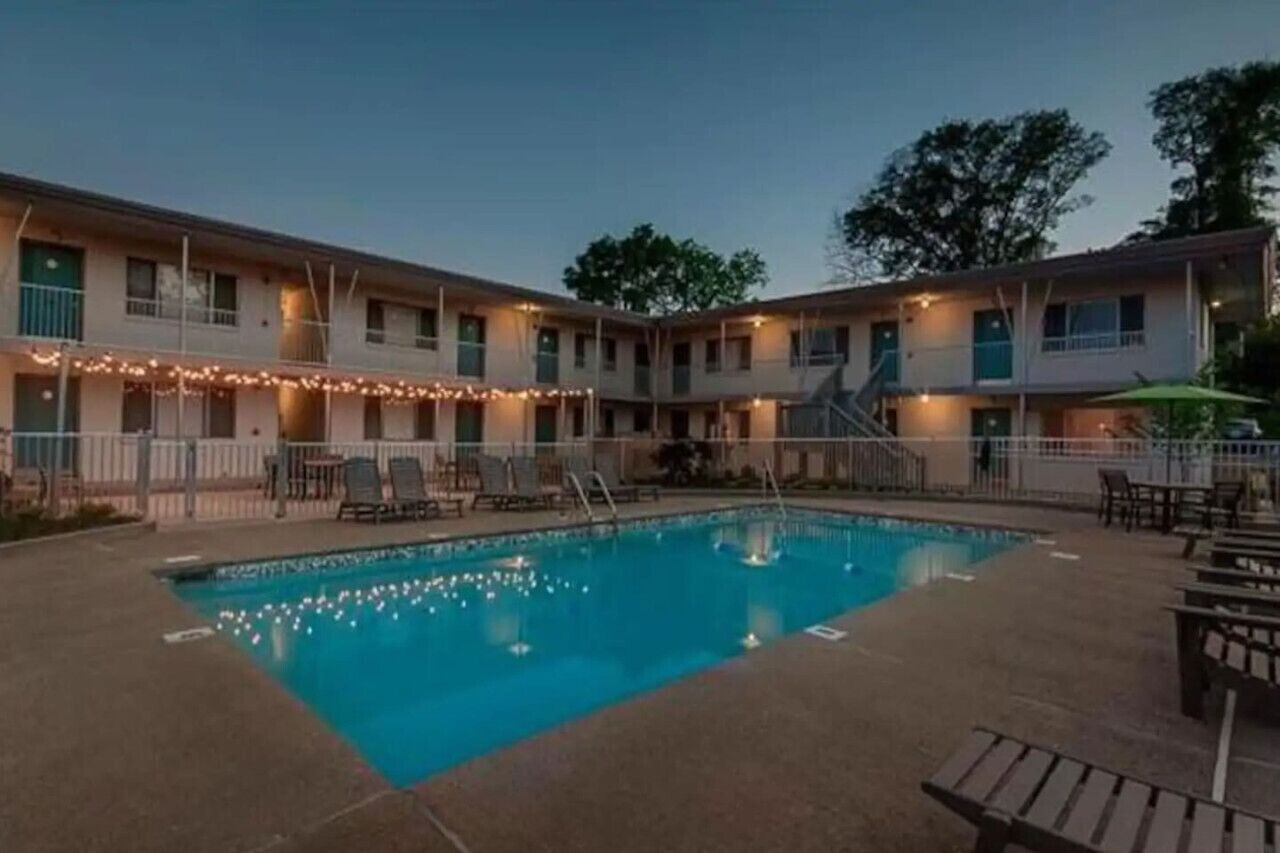 A hotel with a swimming pool, outdoor seating, and a covered patio area.