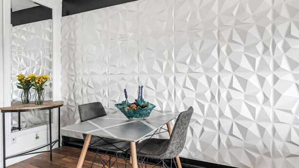 Un comedor con un muro de diseño geométrico, una mesa con sillas y un florero sobre una mesita.
