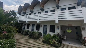 A multi-story building with a white facade, multiple balconies, and a garden area with various plants and a pathway. - Point F Siargao (General Luna)