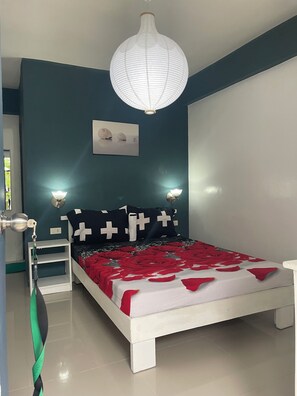 Quarto com cama branca, paredes verde-água, luminária branca no teto e mesa de cabeceira com abajur.