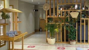 A hotel lobby with a wooden reception desk, potted plants, a patterned ceiling, and a display cabinet with various items. - Shatha Abha Furnished Units (Abha)