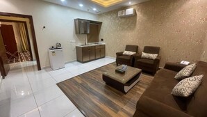 A living room with a sofa set, a coffee table, and a kitchen area with cabinets and a refrigerator. - Shatha Abha Furnished Units (Abha)