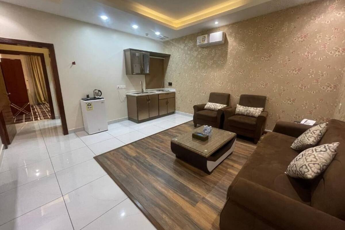 A living room with a sofa set, a coffee table, and a kitchen area with cabinets and a refrigerator.