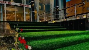 A hotel entrance with a reception desk, a staircase leading to the upper floors, and a well-maintained garden with various plants and flowers. - Shatha Abha Furnished Units (Abha)