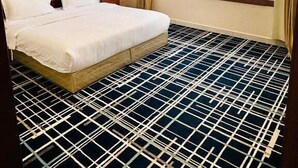 A hotel room with a large bed, a wooden headboard, a window with a city view, and a patterned floor. - Shatha Abha Furnished Units (Abha)