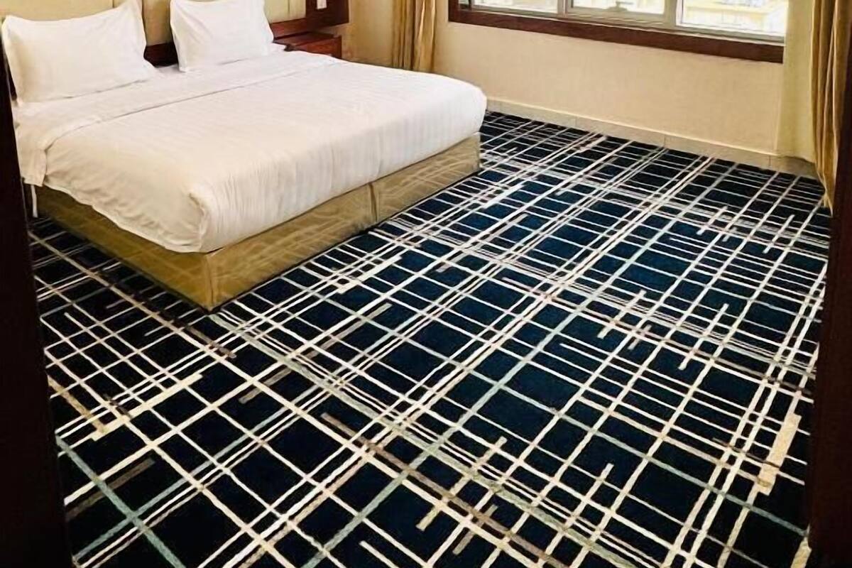 A hotel room with a large bed, a wooden headboard, a window with a city view, and a patterned floor.