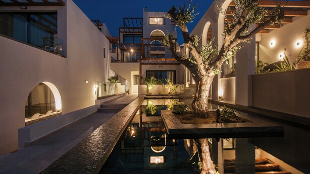 Un edificio moderno con un patio central, una piscina reflectante y un árbol.