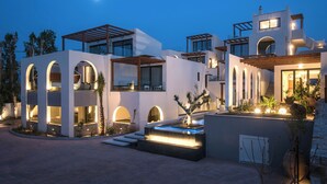 Una casa moderna de varios pisos con piscina, ventanas arqueadas y un cielo iluminado por la luna.