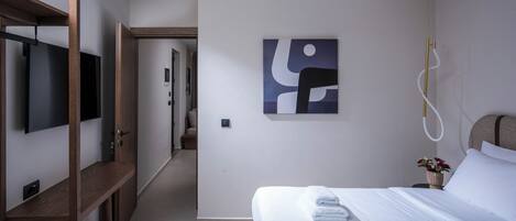 A modern hotel room with a bed, a TV, a ceiling fan, and a painting on the wall.