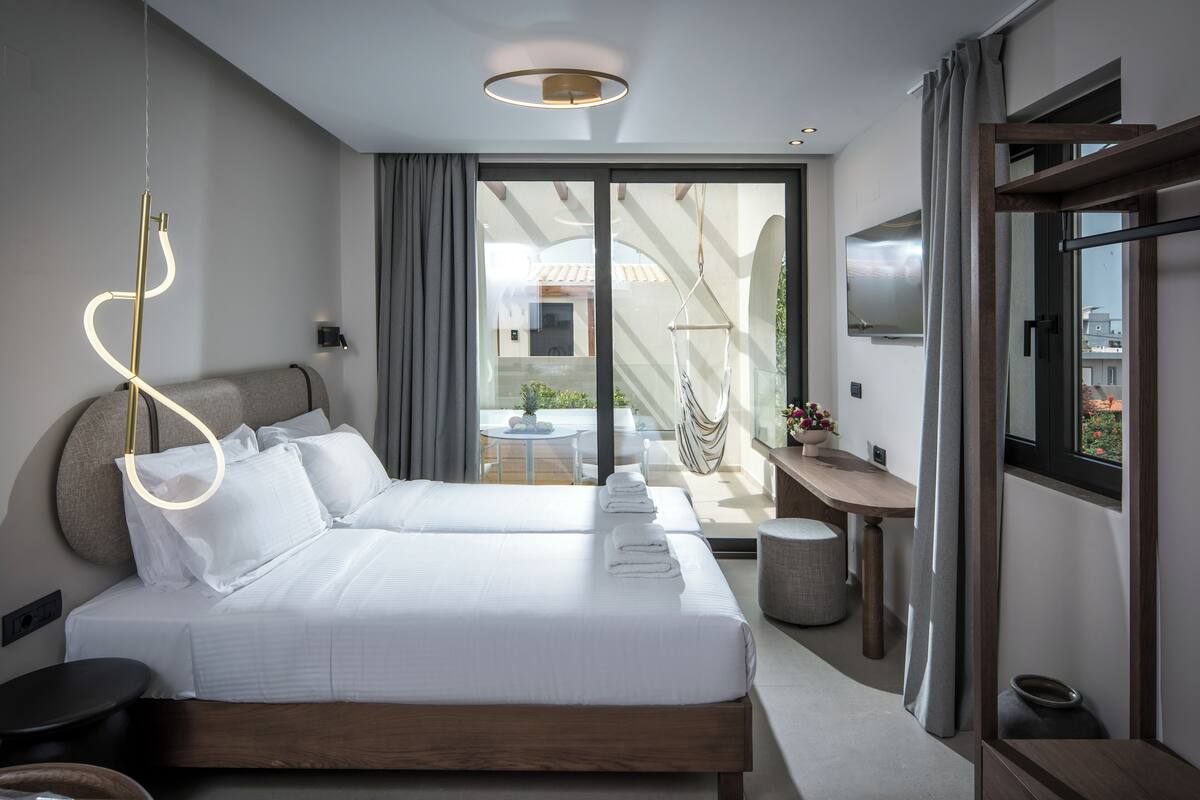 A modern hotel room with two beds, a desk, and a balcony with a view.