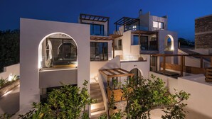 Una casa moderna de varios niveles con una escalera central, ventanas amplias e iluminación exterior.