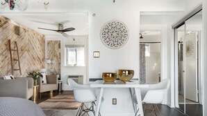 Un salon moderne avec un mur en bois à motifs en chevrons, un canapé blanc, une table à manger agrémentée de deux bols dorés et un ventilateur de plafond.