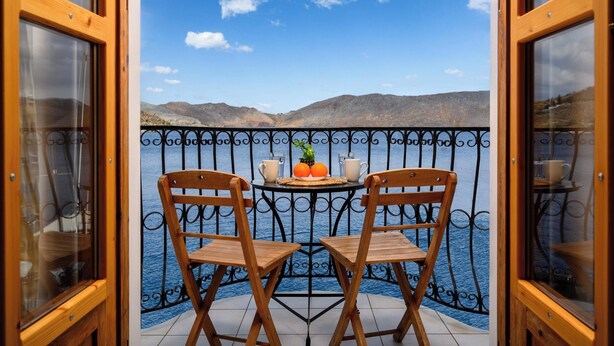 A balcony with two wooden chairs, a small round table, and a view of the sea and mountains. - 1st Floor Grey - Over The Sea Apartments with a sea view (Simi)