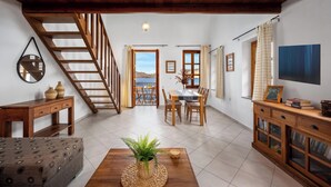A spacious living area with a wooden staircase, a dining table with chairs, a sofa, and a cabinet with glass doors. - 1st Floor Grey - Over The Sea Apartments with a sea view (Simi)