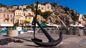 A coastal town with buildings, a prominent anchor sculpture, and boats in the water. - 1st Floor Grey - Over The Sea Apartments with a sea view (Simi)