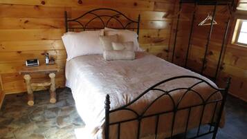 A wooden cabin room with a stone floor, a metal bed frame, and a small bedside table with a phone.