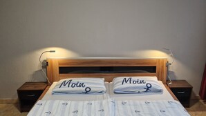 A neatly made bed with two pillows, each labeled "Moin," a wooden headboard, bedside tables, and a window with red curtains. - FeWo SN-Zippendorf with sauna, close to the beach and 4 km to the Citty (Schwerin)