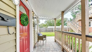 A covered porch with a red door, a welcome mat, and a wicker chair. - Cozy Jacksonville Cottage, Walkable Location! (Jacksonville)