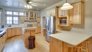 A spacious kitchen with wooden cabinets, a stainless steel refrigerator, a ceiling fan, and a large window providing natural light.