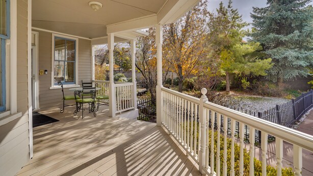 A covered porch with a wooden floor, a ceiling fan, and a view of trees and a fence.