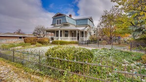 A two-story house with a porch, surrounded by a garden and a fence.