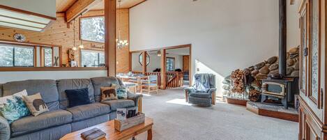 A spacious living room with a wooden ceiling, a sofa with cushions, a coffee table, and a fireplace with logs.