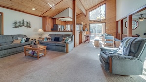 A spacious living area with a large sofa, a recliner, and a coffee table. There is a kitchen area with wooden cabinets and a dining table. - Home 1 Mi to Downhill Ski Resort: Bring Your Pets! (Truckee)