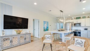 A modern kitchen with white cabinets, a large island, and a flat-screen TV. - Steps to Beach: Pet-friendly Crystal Beach Home (Port Bolivar)