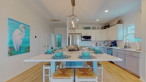 A modern kitchen with white cabinetry, a large island with teal accents, and a painting of a bird on the wall. - Steps to Beach: Pet-friendly Crystal Beach Home (Port Bolivar)