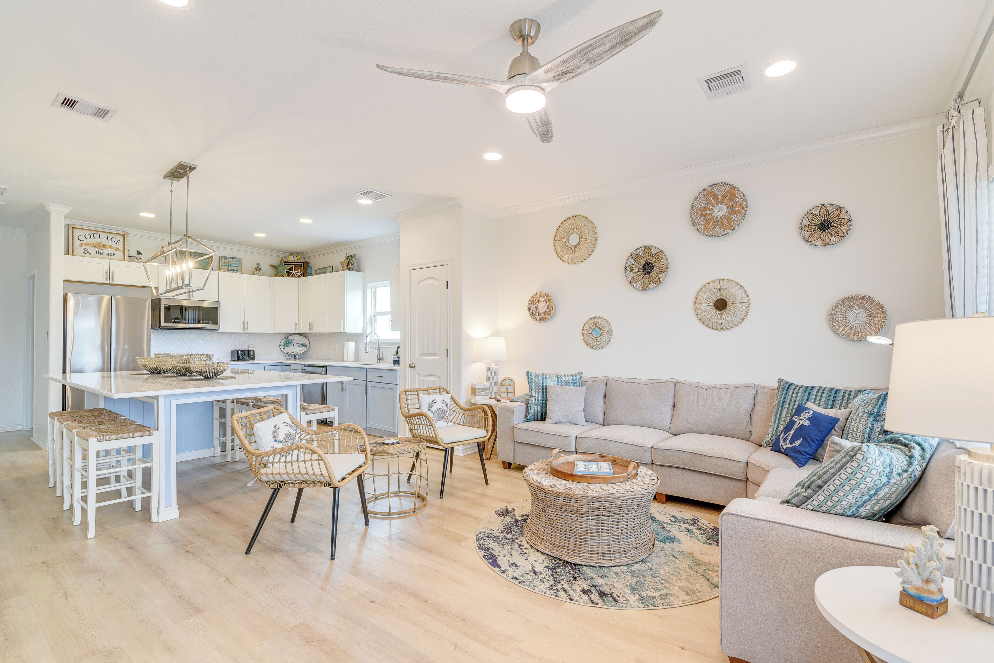 Una cocina moderna con armarios blancos, una isla central y una zona de comedor con sillas de mimbre.