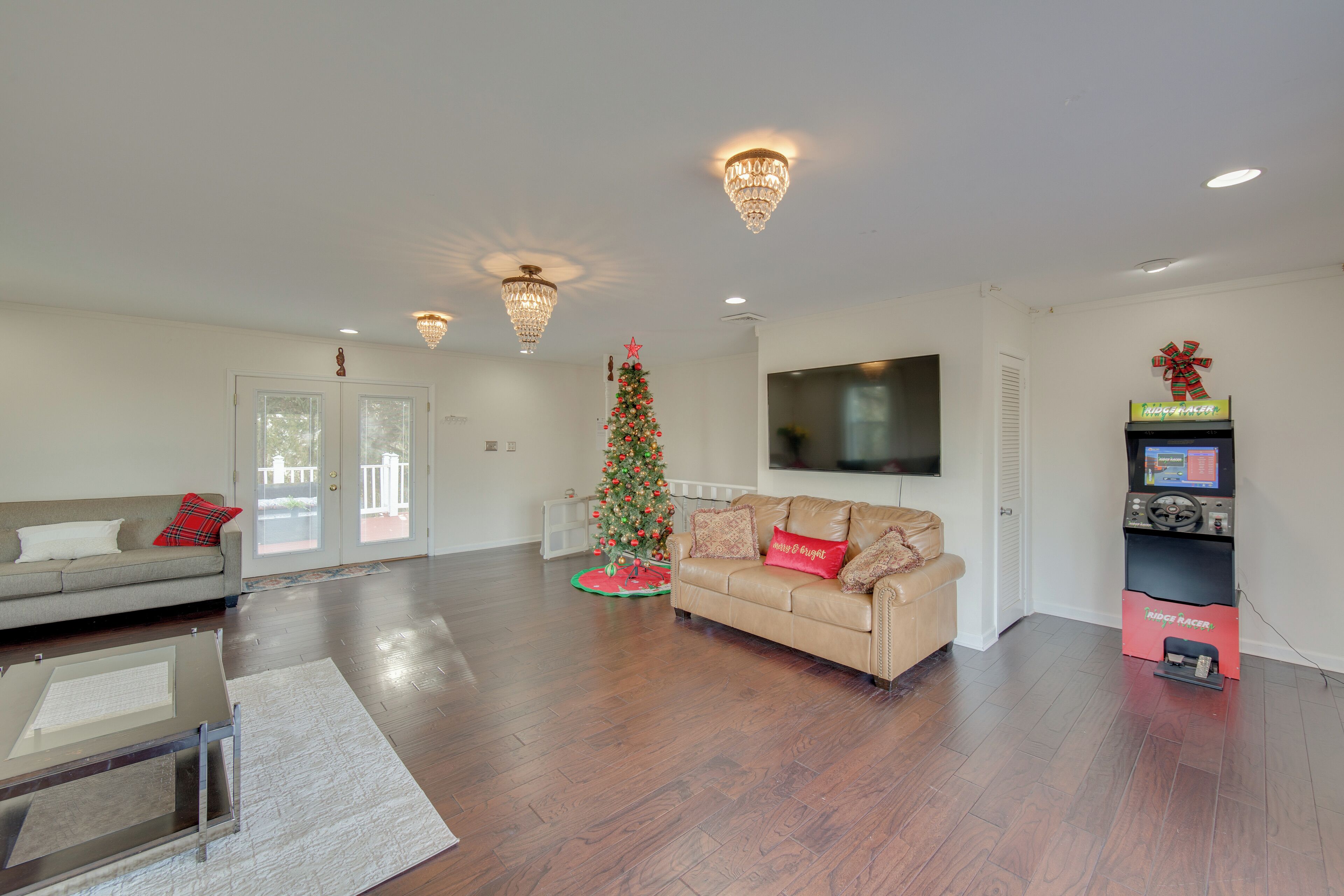 A modern living room with a large flat-screen TV, a Christmas tree, and a beige sofa.