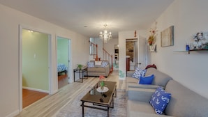 A spacious living room with a sofa, coffee table, and a chandelier. There is a staircase leading to another level, and a door leading to a bedroom. - 2 Mi to Hersheypark: Group Getaway w/ Deck (Hummelstown)