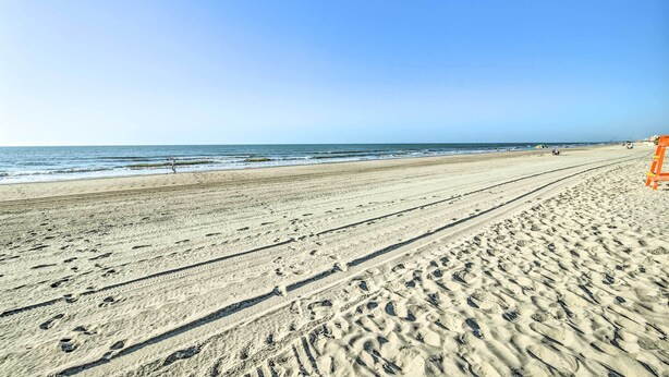 Une vaste plage de sable, parsemée d’empreintes, sous un ciel dégagé.