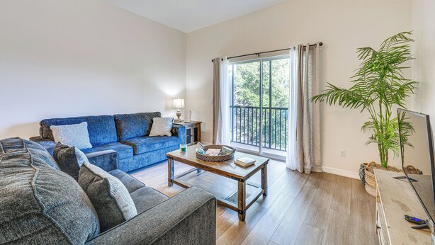 Ein Wohnzimmer mit einem blauen Sofa, einem grauen Sofa, einem Holztisch, einem Fernseher und einem großen Fenster mit Vorhängen.