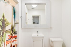 A bathroom with a white sink, a toilet, and a mirror above the sink. - Galveston Vacation Rental Near Cruise Terminals! (Galveston)