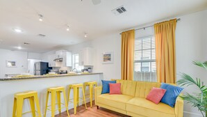 Un salón luminoso con un sofá amarillo, taburetes amarillos y un ventanal con cortinas amarillas.