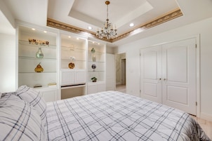 A bedroom with a large bed, built-in shelving with decorative items, a chandelier, and white doors.