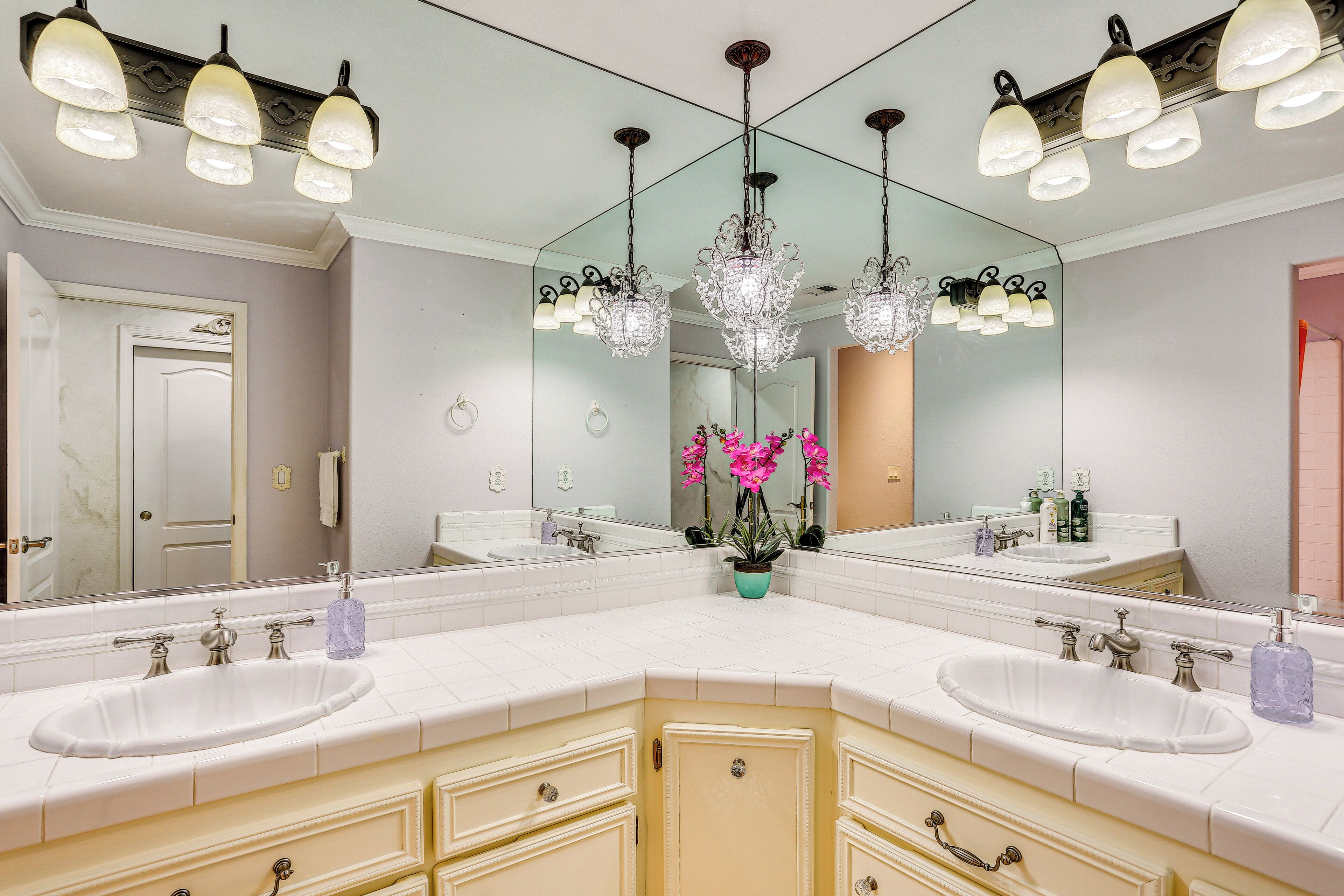Une salle de bain avec deux lavabos, un grand miroir et un lustre.