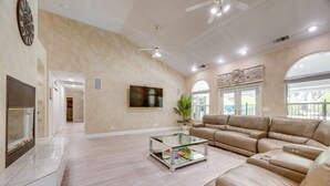 Un salón amplio con un sofá beige, una mesa de centro de cristal, un televisor de pantalla plana y una chimenea.