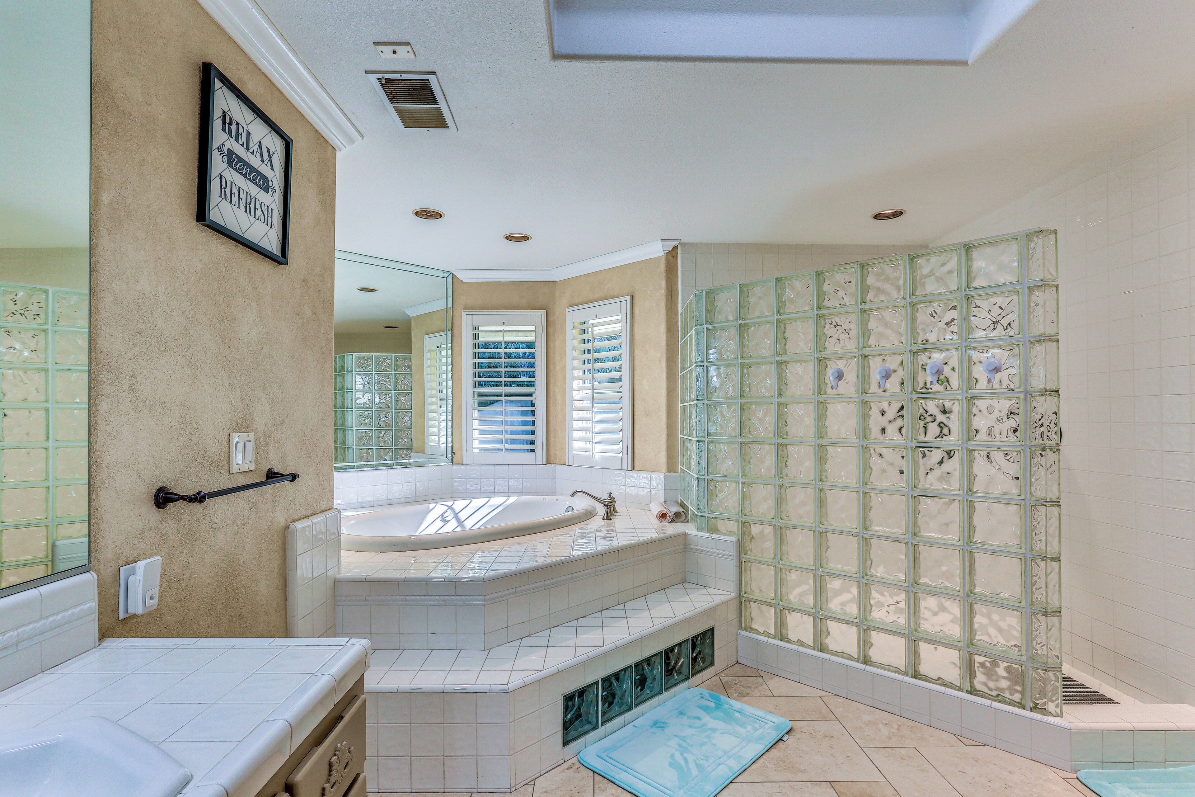 Une salle de bain dotée d’une grande baignoire, d’une douche avec des parois en verre dépoli et d’un meuble-lavabo avec un miroir.