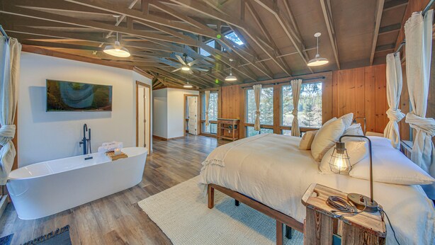 A spacious bedroom with a large bed, a modern bathtub, and a wooden ceiling.