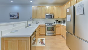 A modern kitchen with wooden cabinets, stainless steel appliances, a white countertop, and a wooden floor. - Crow Creek Golf Club Condo w/ Community Perks! (Calabash)
