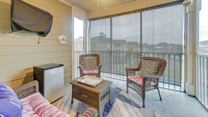 A room with a large window, wicker furniture, a small refrigerator, and a flat-screen TV mounted on the wall. - Crow Creek Golf Club Condo w/ Community Perks! (Calabash)