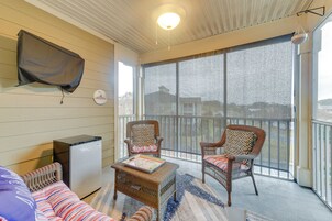 A room with a large window, wicker furniture, a small refrigerator, and a flat-screen TV mounted on the wall.
