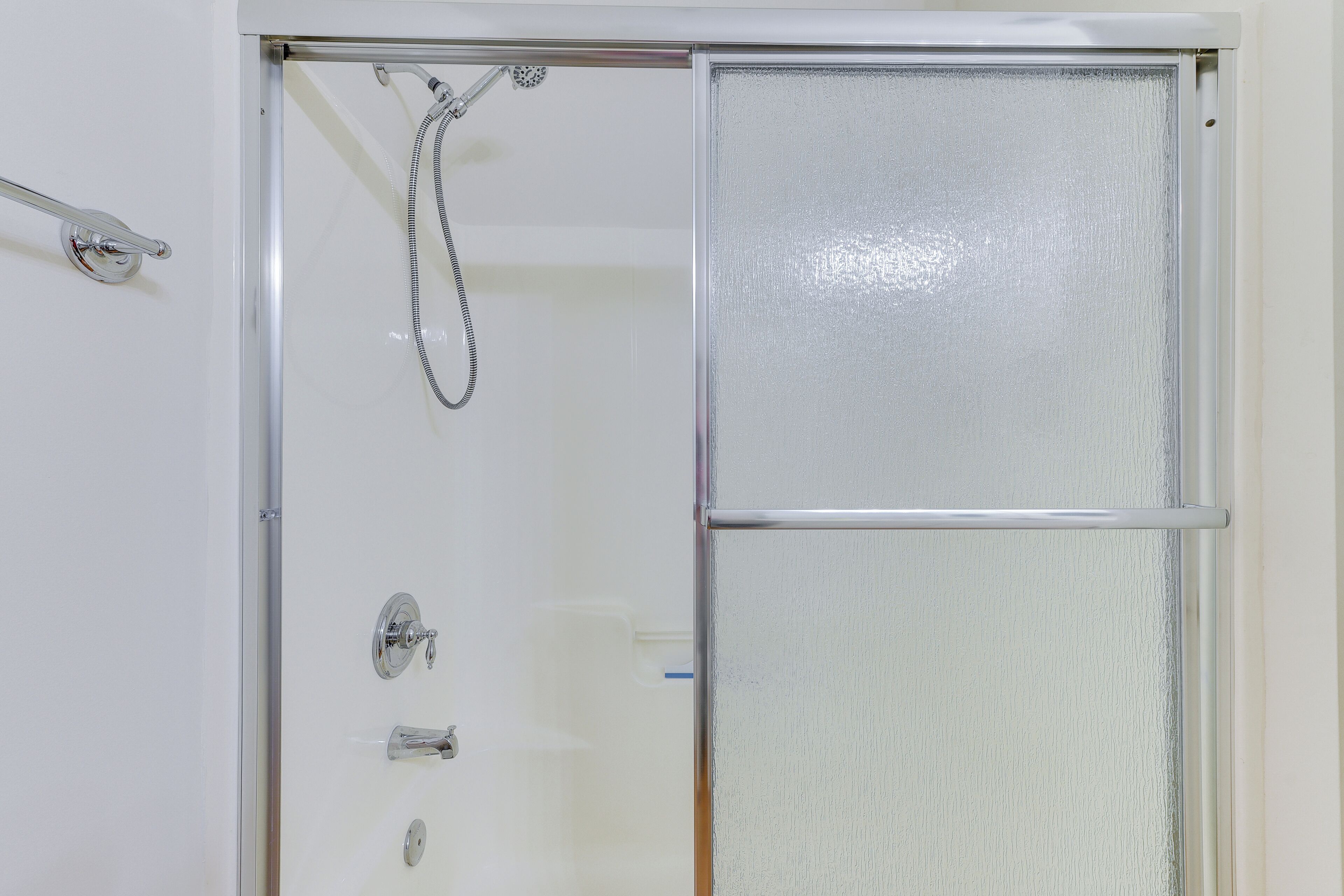 Box de chuveiro com porta de vidro, chuveiro manual e torneira na parede.