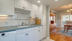 A modern kitchen with white cabinets, a Bosch dishwasher, and a wooden dining table with chairs. - Scituate Vacation Rental - Walk to the Beach! (Scituate)